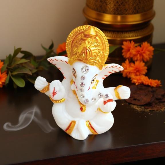 Decorative statue of ganeshji with gold and white colors on a dark surface with flowers in the background.