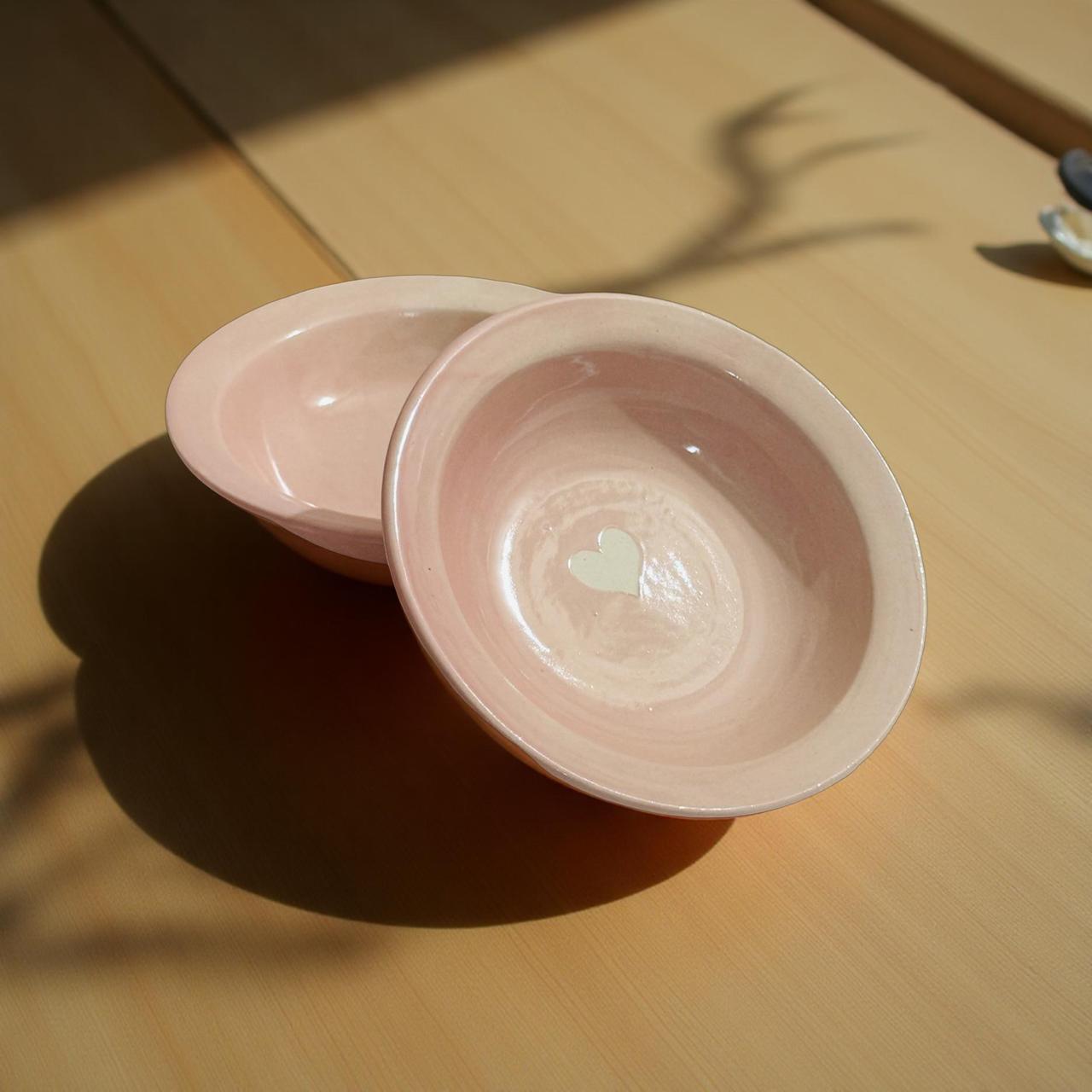 Two pink ceramic bowls with a heart design on a wooden surface.