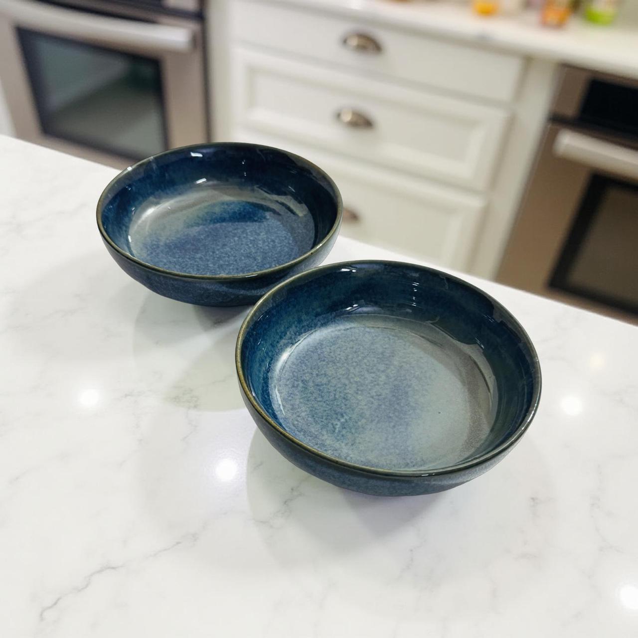 Two blue ceramic bowls on a marble countertop with a kitchen background.
