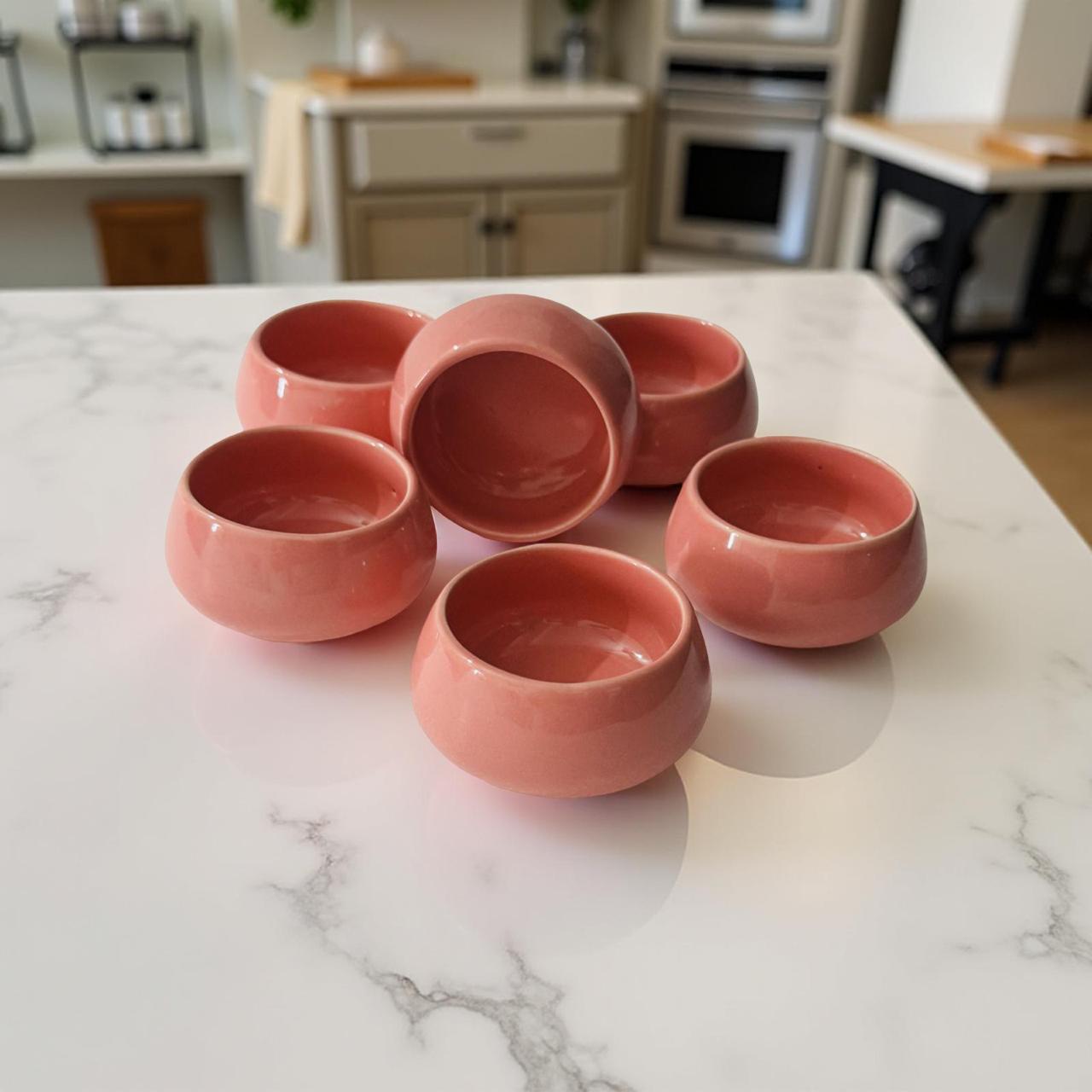 Set of six pink ceramic bowls on a marble countertop with a kitchen background.