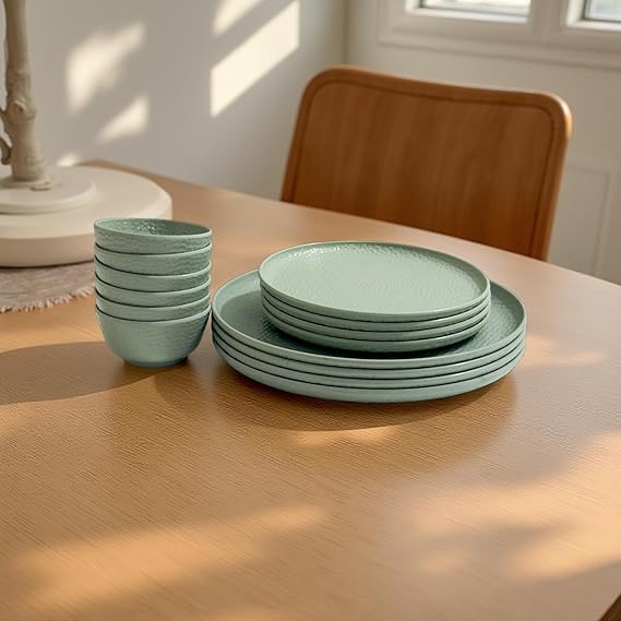 Set of green ceramic plates and bowls on a wooden table with a chair in the background.