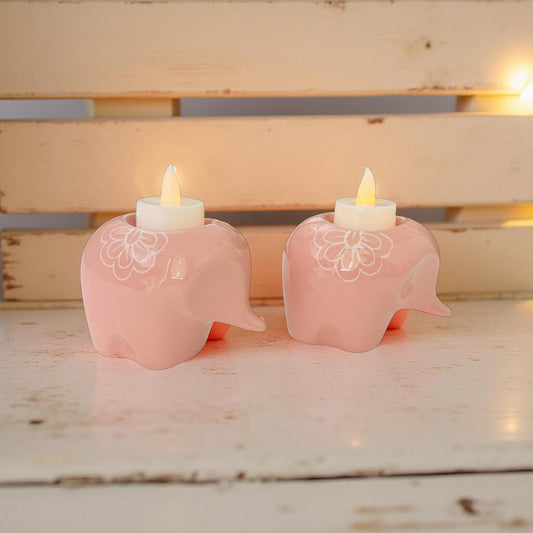 two baby pink elephant t light holders with lit diyas on a wooden platform