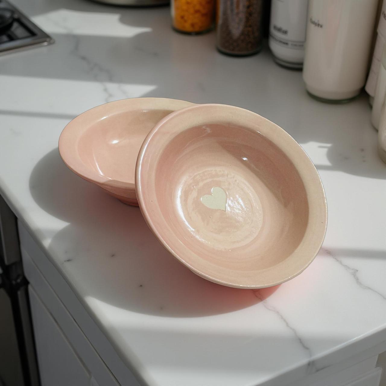 Blush pink ceramic bowls with heart design placed on a kitchen counter in sunlight