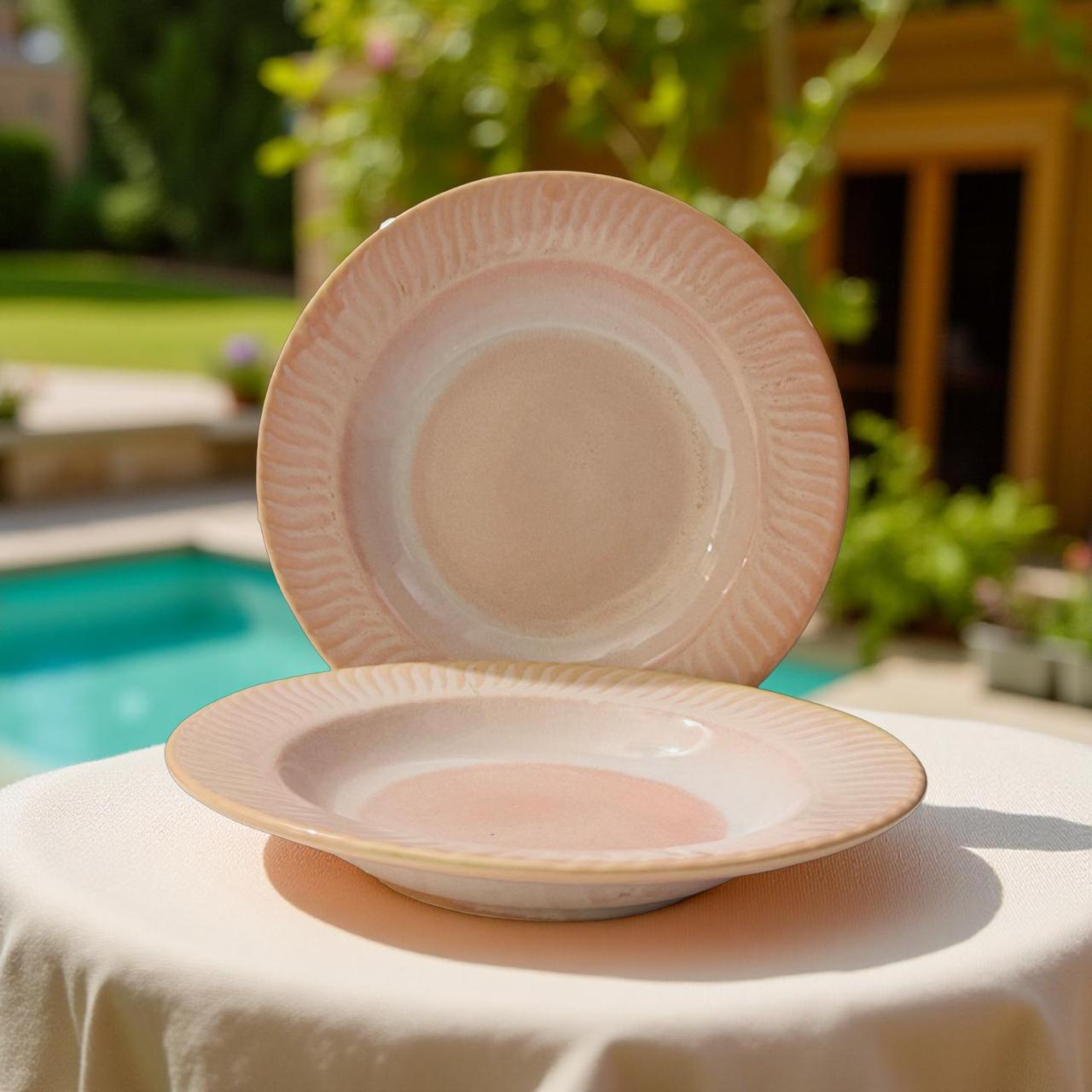 Two pink ceramic plates on a table with a pool and garden in the background