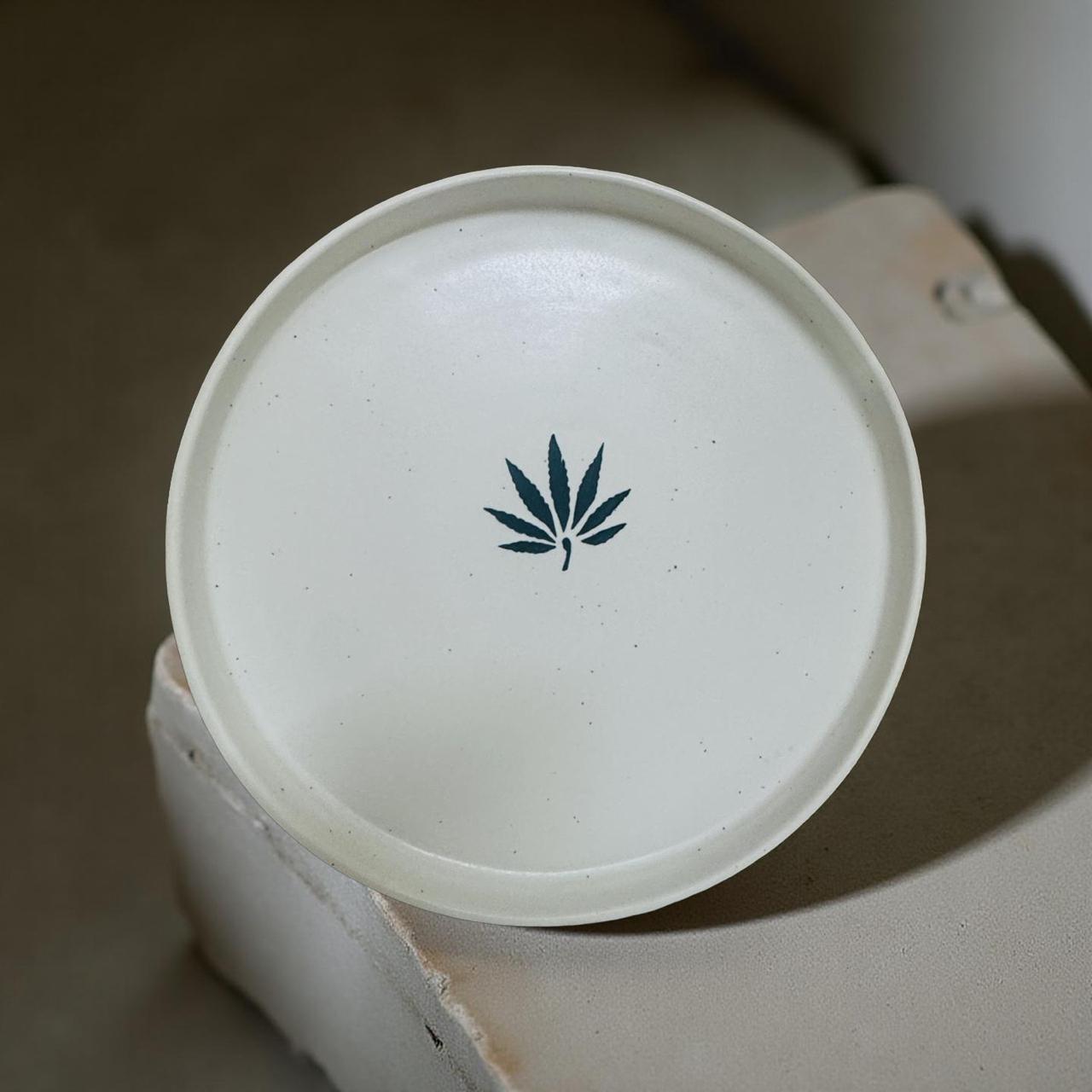 White ceramic plate featuring a cannabis leaf design on a neutral background