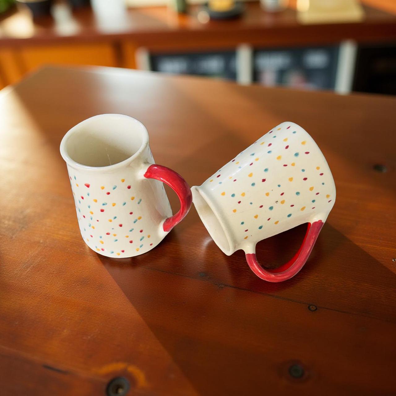 Two polka dot mugs with red handles on a wooden table