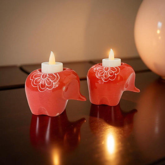 Two red elephant-shaped candle holders with lit candles on a reflective surface.