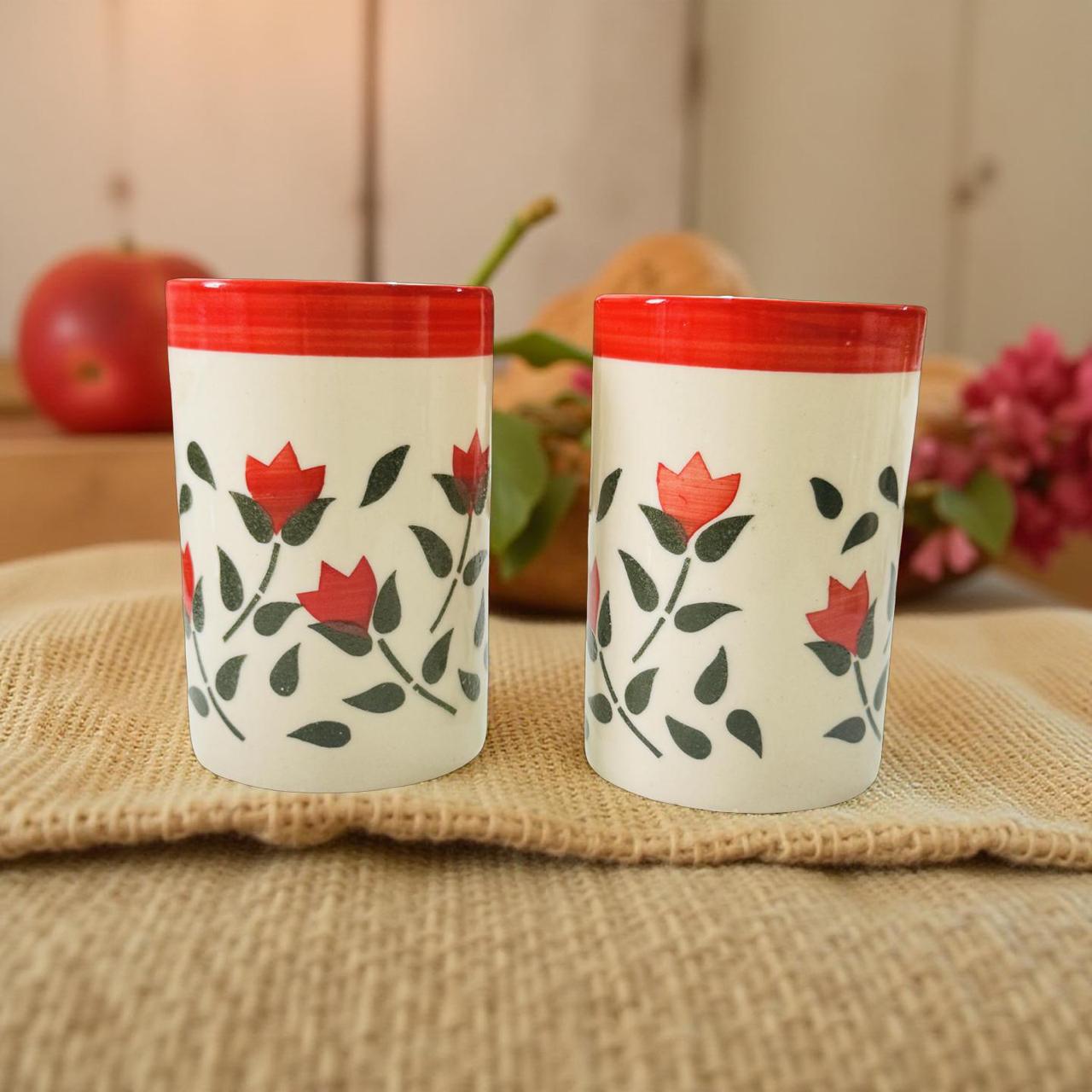 Two ceramic tumblers with red floral design on a woven mat