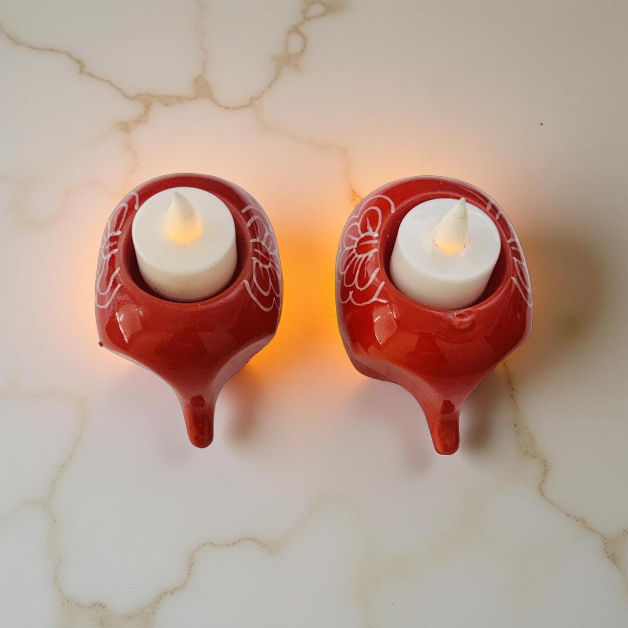 Two red ceramic wall sconces with white candle-like lights on a marble surface.