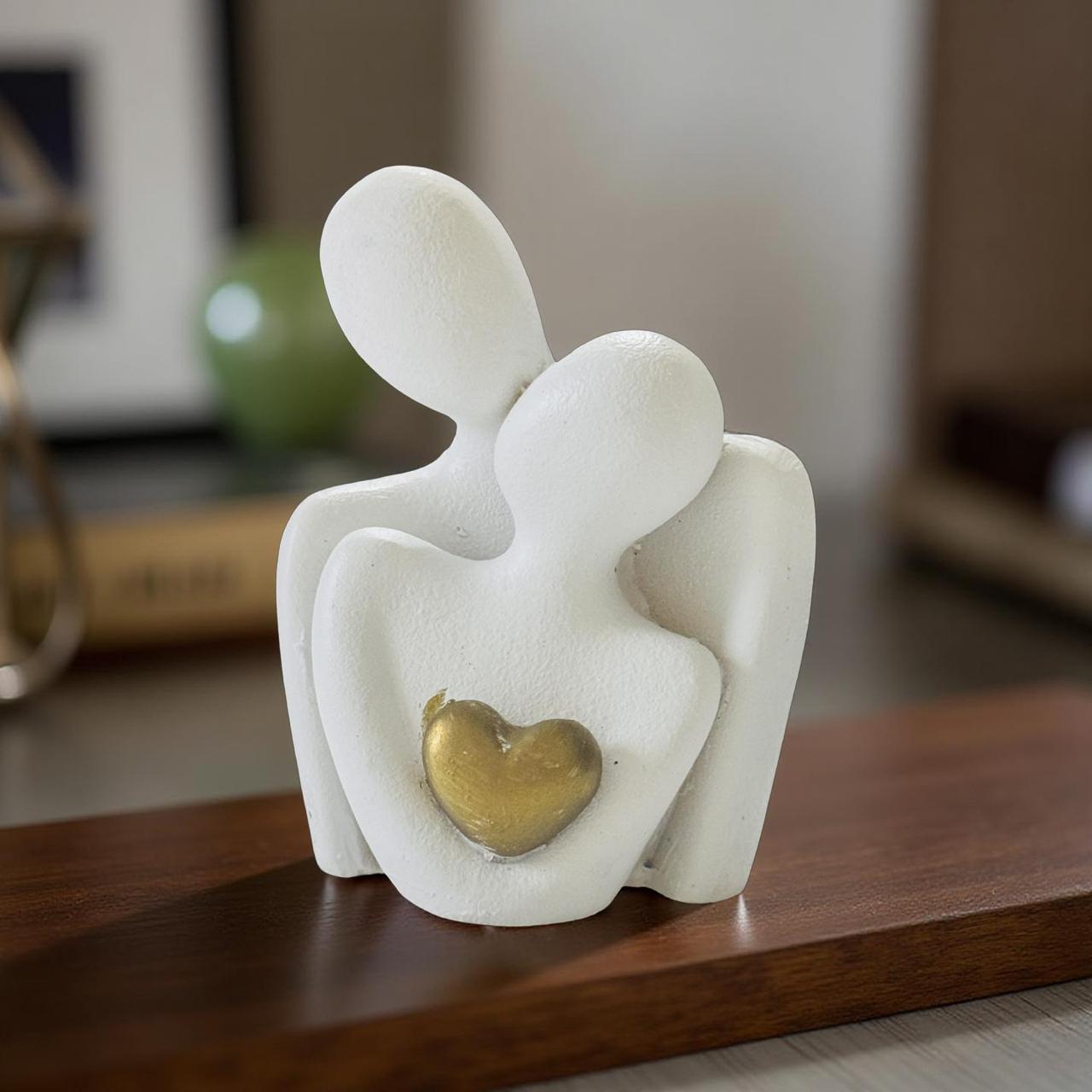 White marble sculpture of two figures holding a gold heart on a wooden surface.
