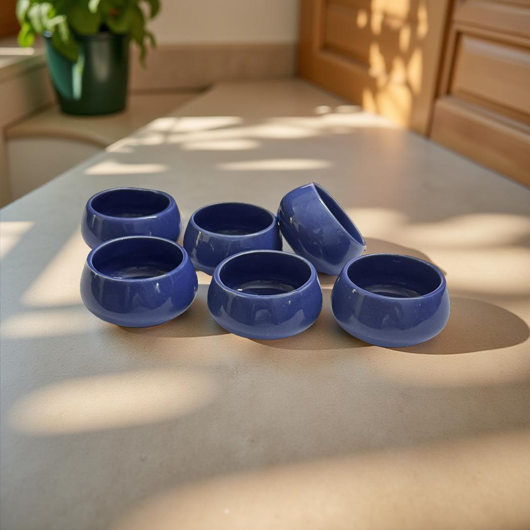 Set of six blue ceramic bowls on a light-colored surface with a plant in the background.