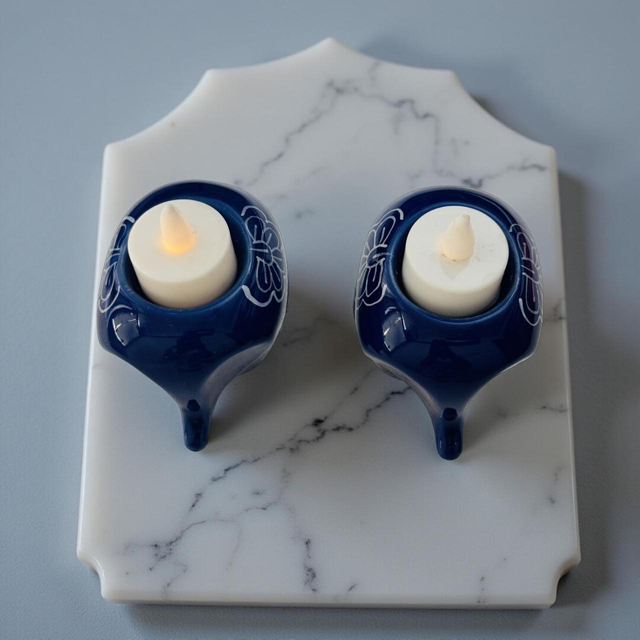 Two blue ceramic candle holders with lit candles on a marble surface