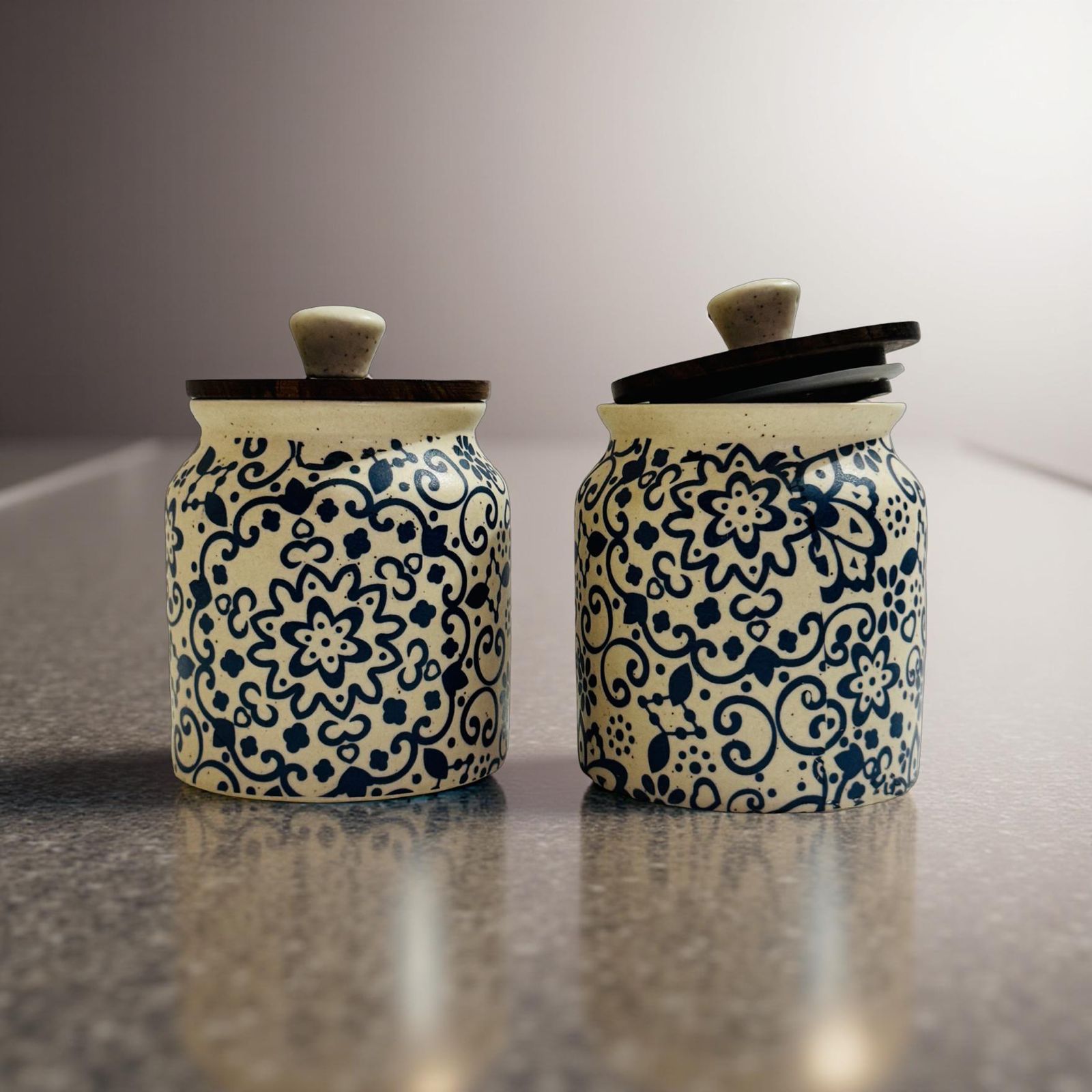 two handpainted ceramic jars with wooden lid placed on a granite stone surface