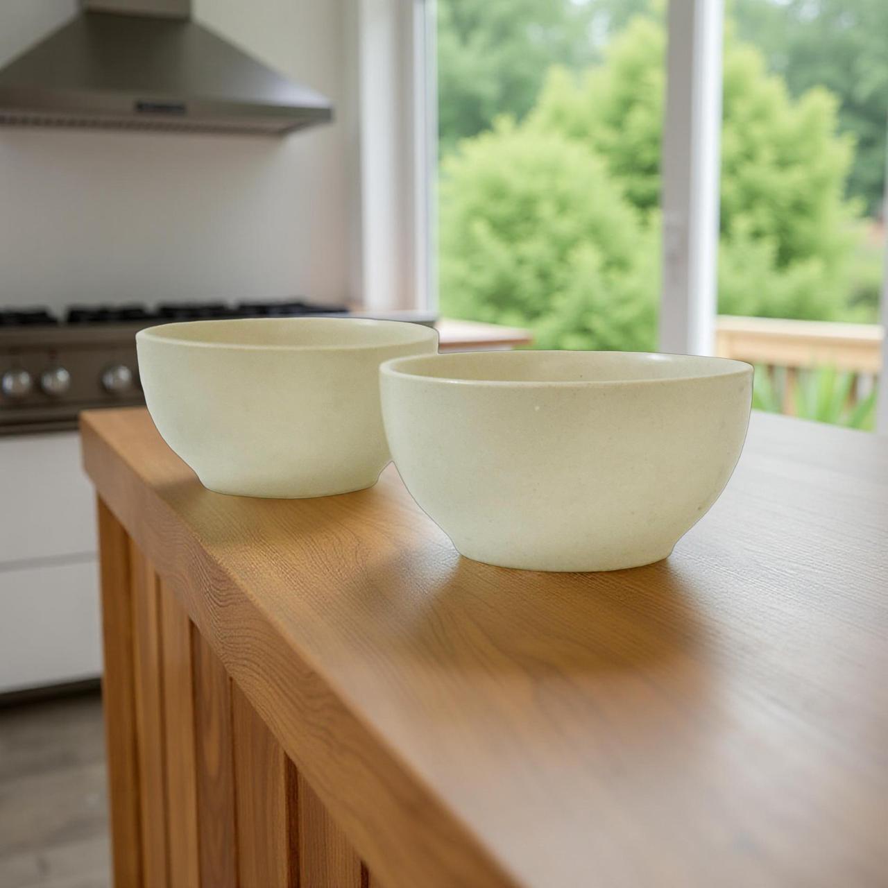 Two white bowls on a wooden kitchen counter with a blurred green outdoor view.