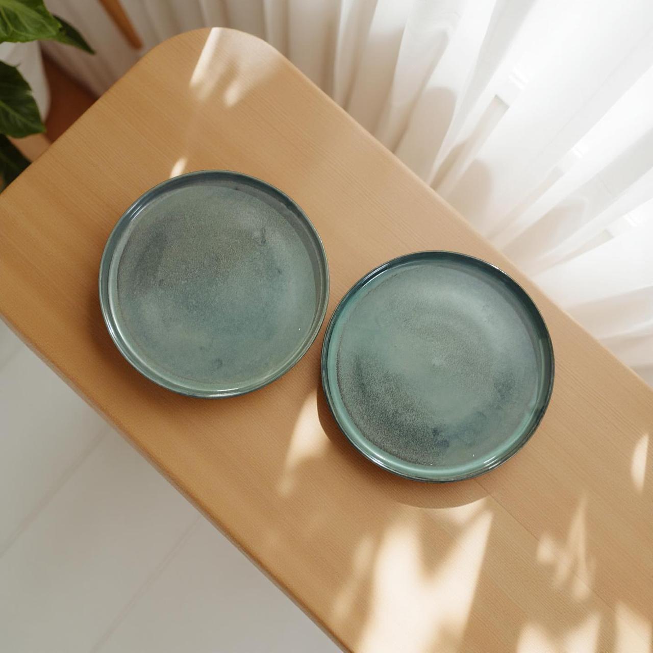 Two green ceramic plates on a wooden surface with sunlight casting shadows.