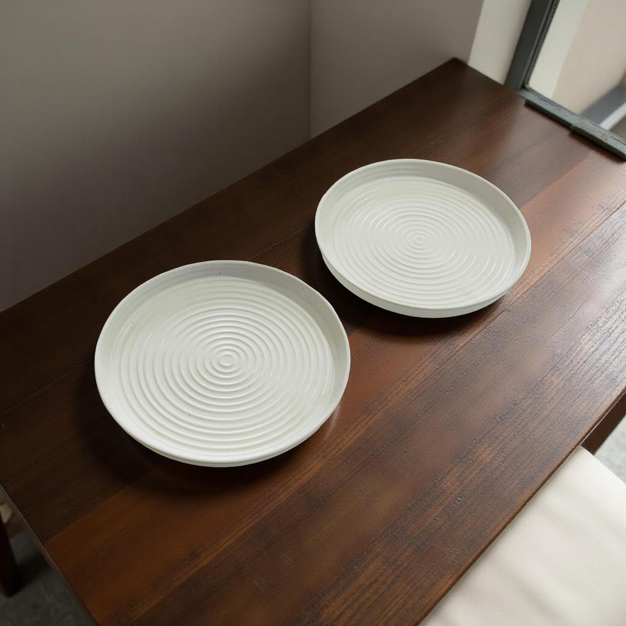 Two white ceramic plates with textured design on a wooden surface.