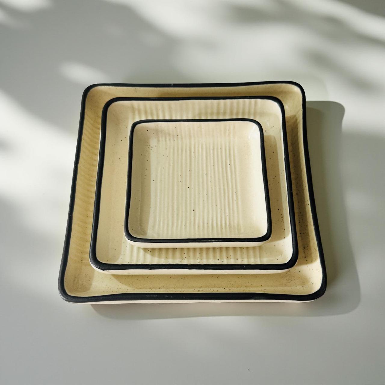 Set of square ceramic plates with black rims on a light background
