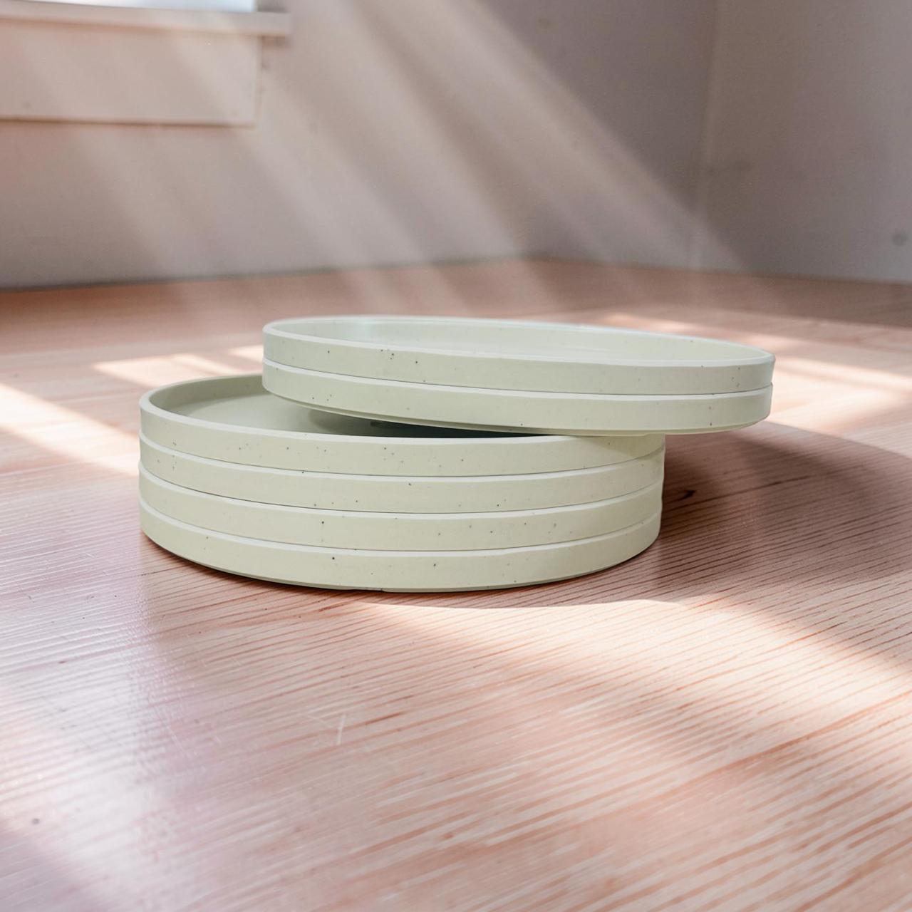 Set of light green ceramic plates stacked on a wooden surface with soft shadows.