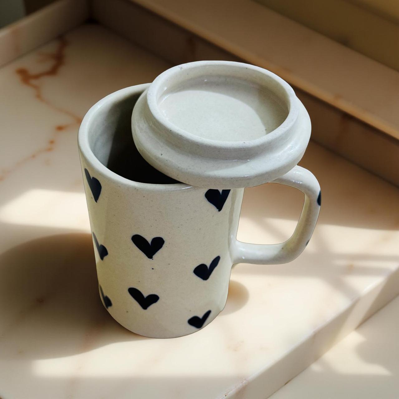 White mug with black heart patterns and a white lid on a light surface.