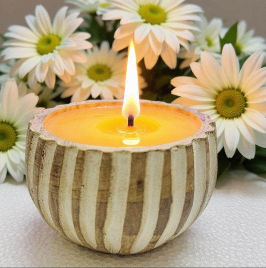 Candle in a striped container with flowers in the background