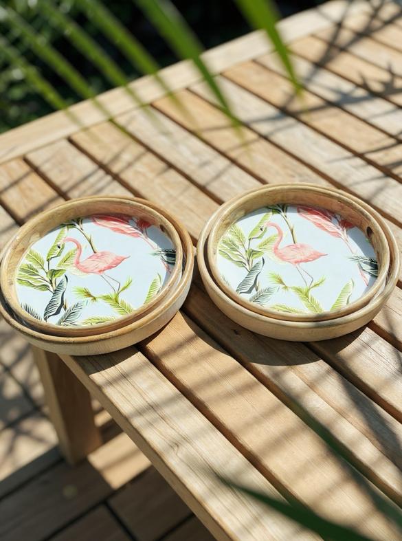 Two round trays with flamingo design in bamboo holders on a wooden surface.
