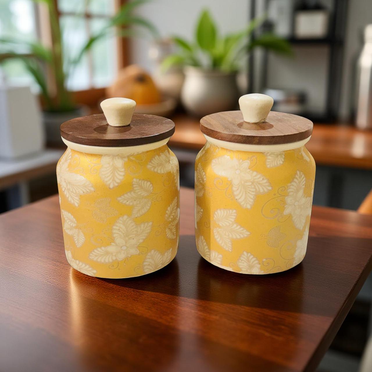 Two ceramic jars with wooden lids on a wooden table in a kitchen setting.