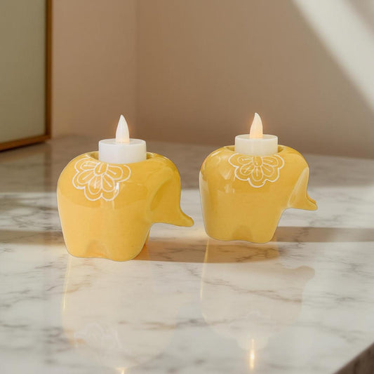 Two yellow elephant-shaped candle holders with lit candles on a marble surface.