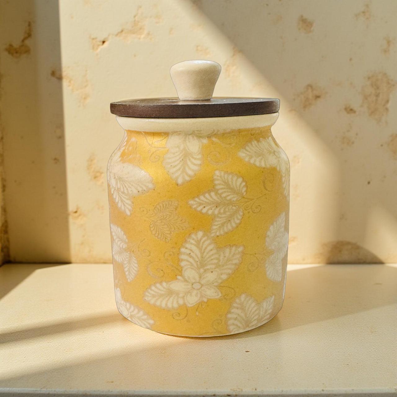 Yellow ceramic jar with white floral patterns and a wooden lid on a light surface.