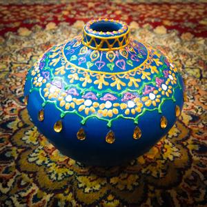 blue terracotta vase with meenakari work placed on a silk woolen carpet