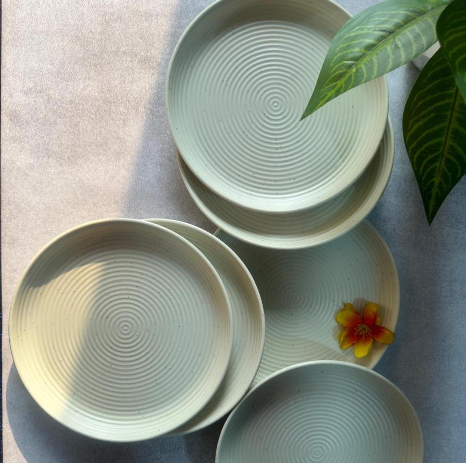A set of pastel green melamine quarter plates with a geometric pattern, displayed on a table with a few decorative flowers added to one of the plates.
