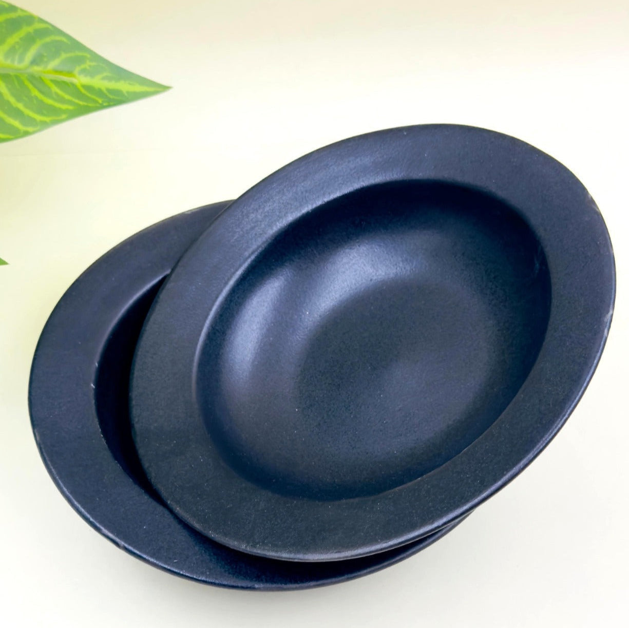 A set of two matte black ceramic deep pasta plates placed one inside the other.