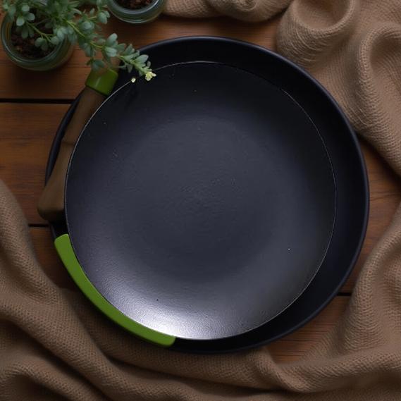 Black frying pan with green handle on a wooden surface
