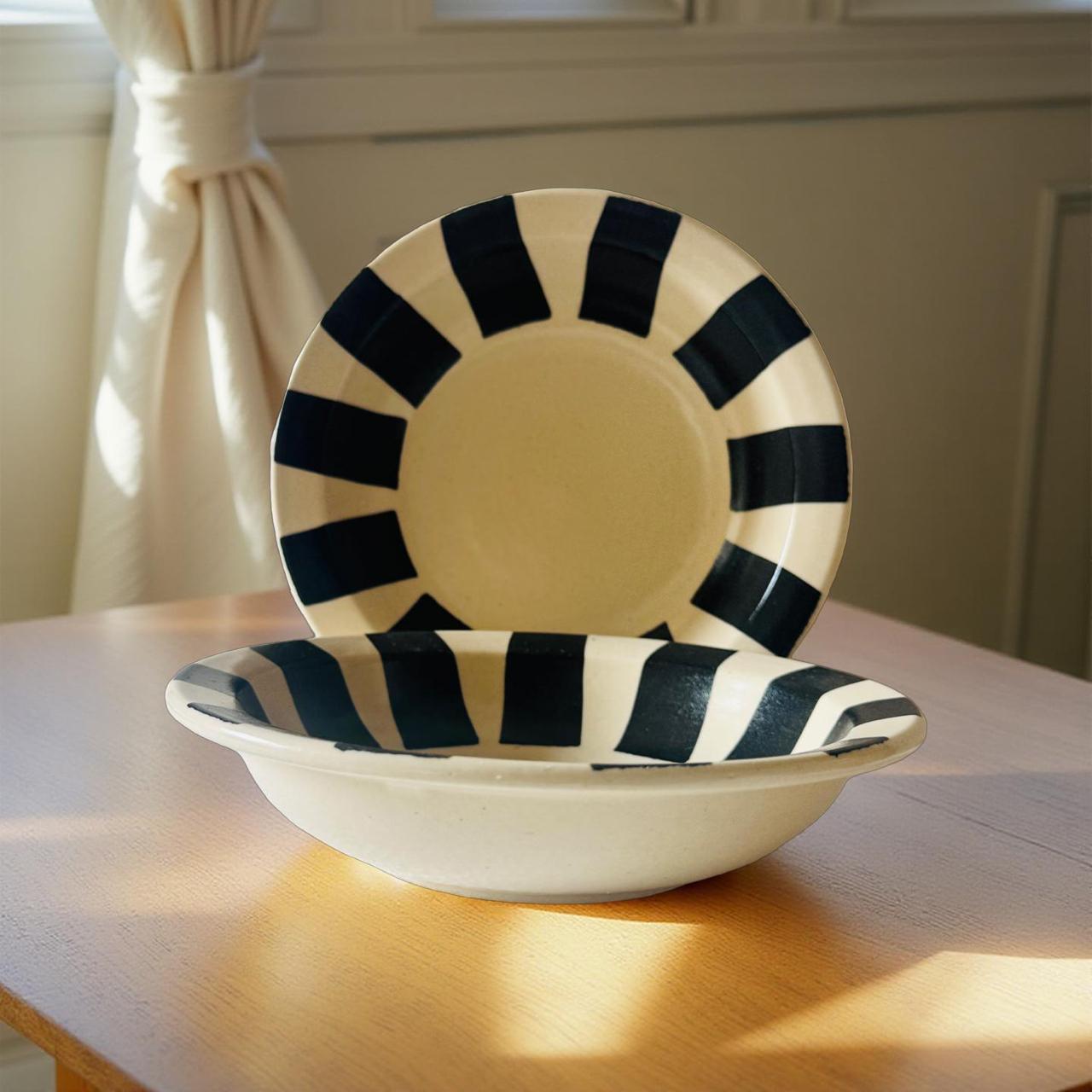 Ceramic bowl and plate with black and white striped design on a wooden table.