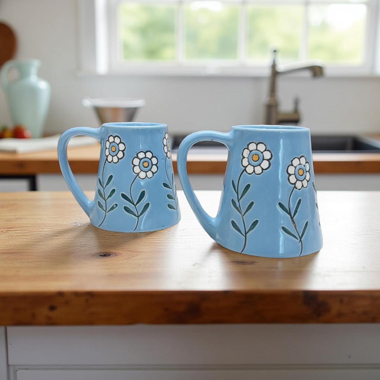 Two blue mugs with floral designs on a wooden kitchen counter.