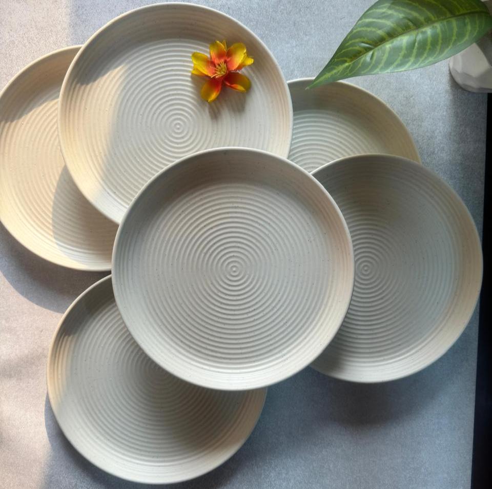 A set of beige round melamine quarter plates displayed on a table, with a decorative flower in the center.