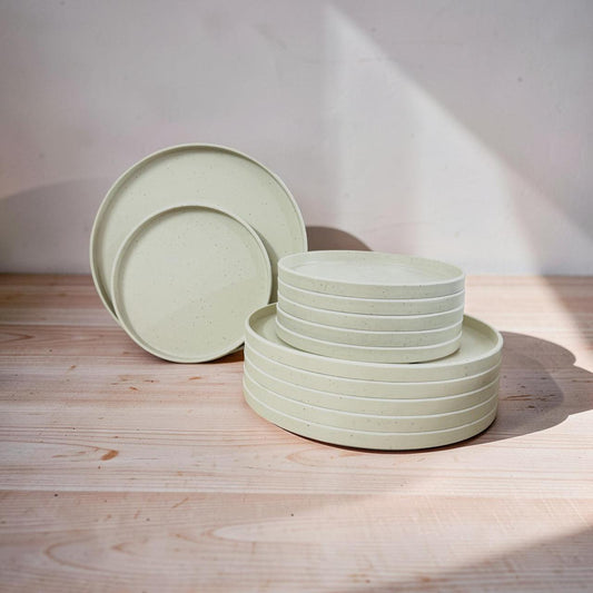 Set of light green ceramic plates and bowls on a wooden surface with a neutral background