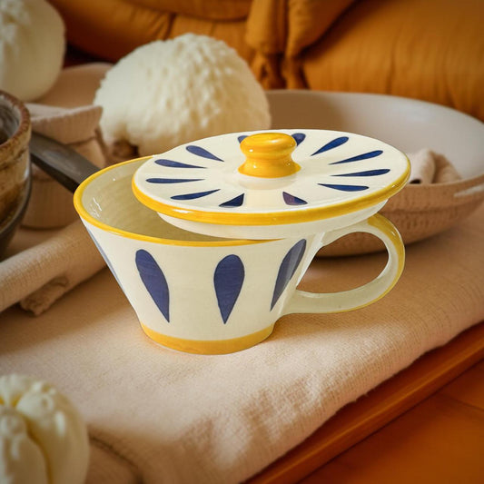 Decorative mug with blue patterns and a yellow handle on a soft surface.