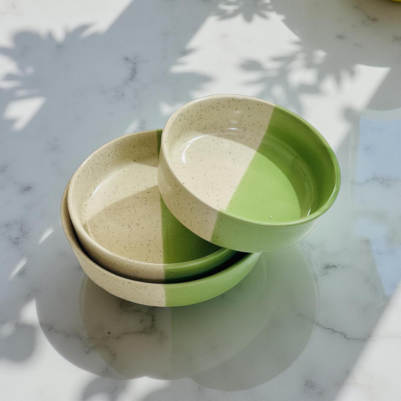 Two green and beige ceramic bowls stacked on a marble surface with shadows from leaves.
