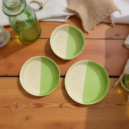Three ceramic plates with green and beige design on a wooden surface.