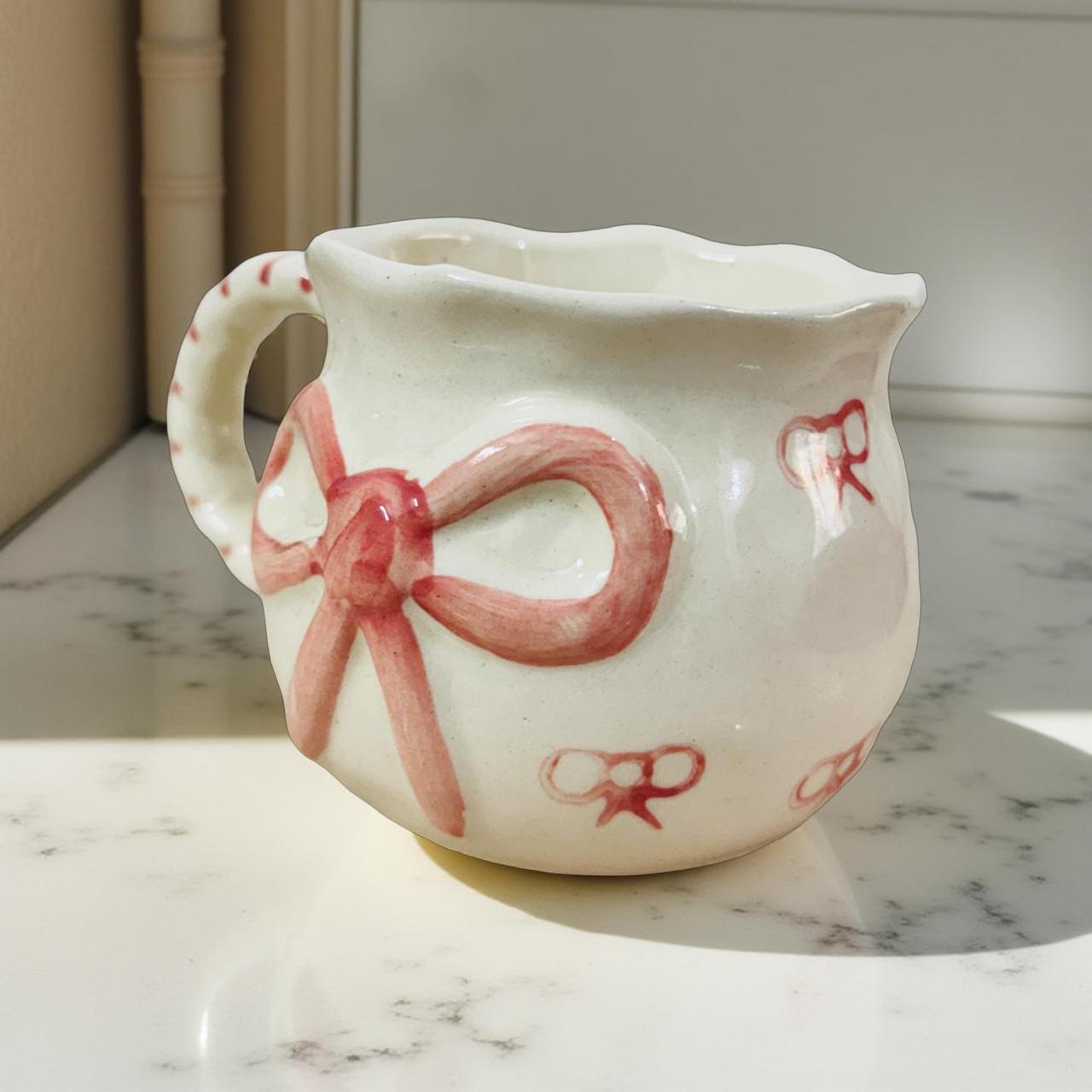 White ceramic mug with red bow design on a marble surface