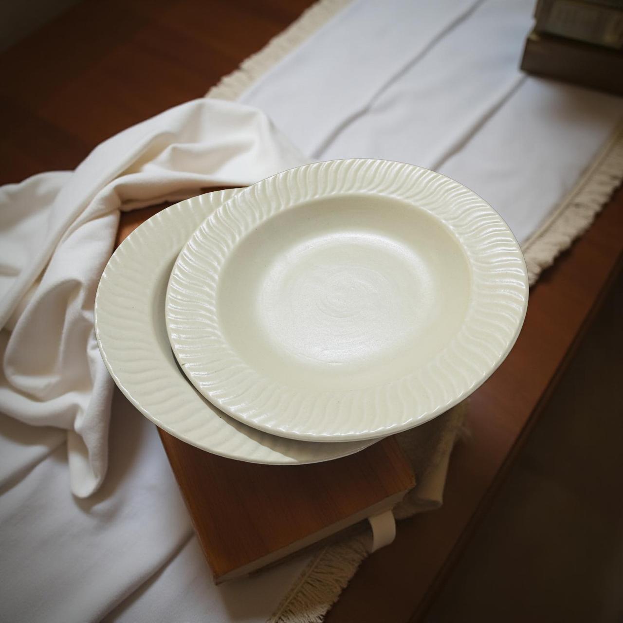 Two white ceramic plates stacked on a wooden surface with a white cloth in the background.