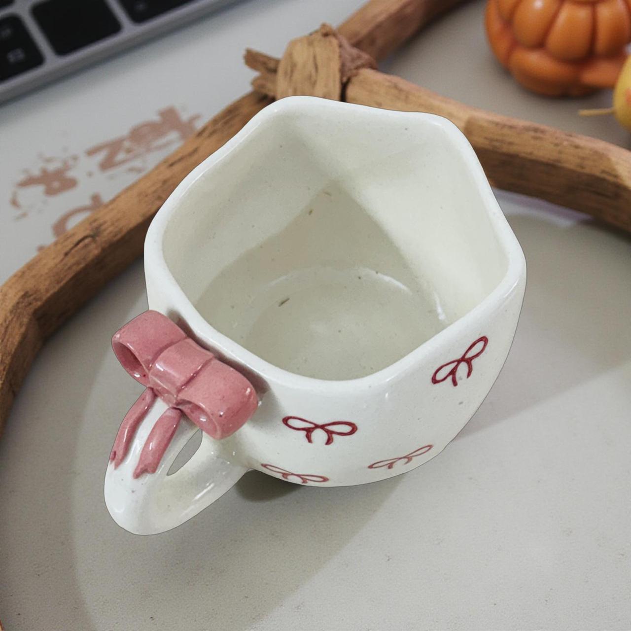 White ceramic cup with pink handle and decorative elements on a light surface.