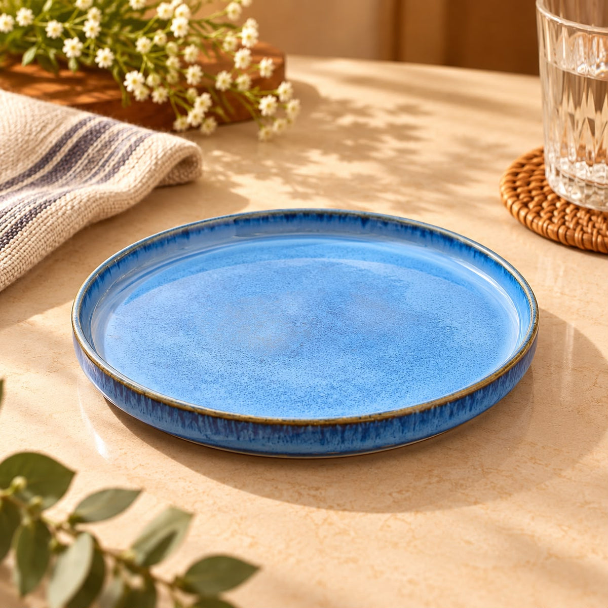 Round blue ceramic plate displayed on a beige dining table with flowers and glassware