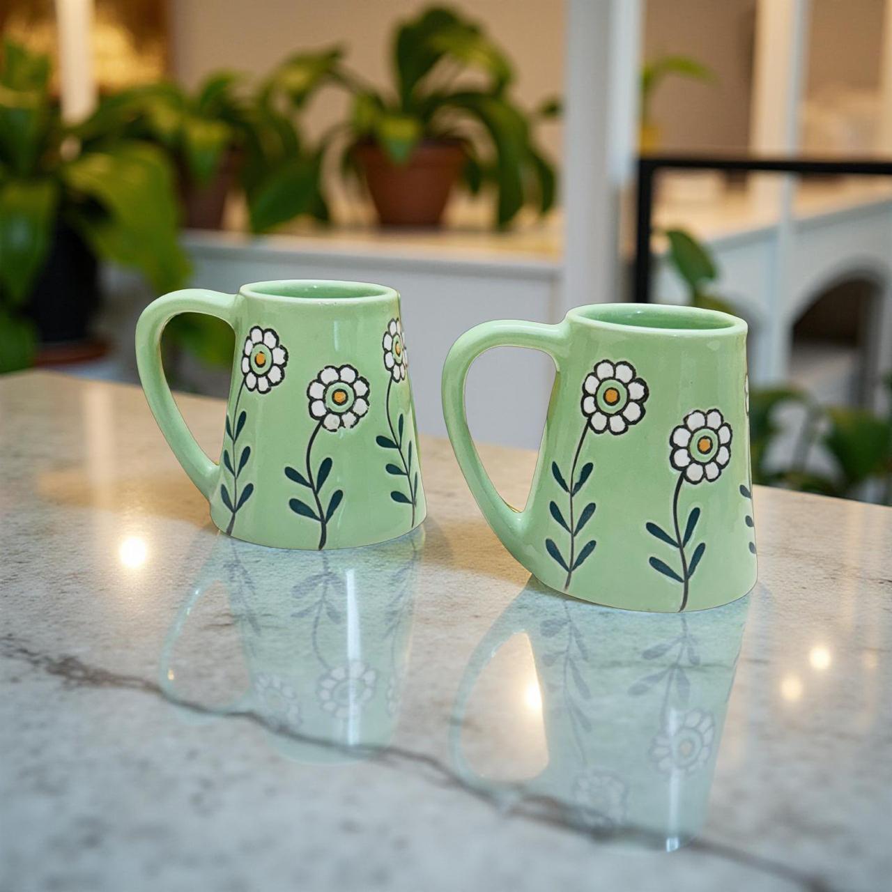 Two green mugs with floral designs on a marble surface.