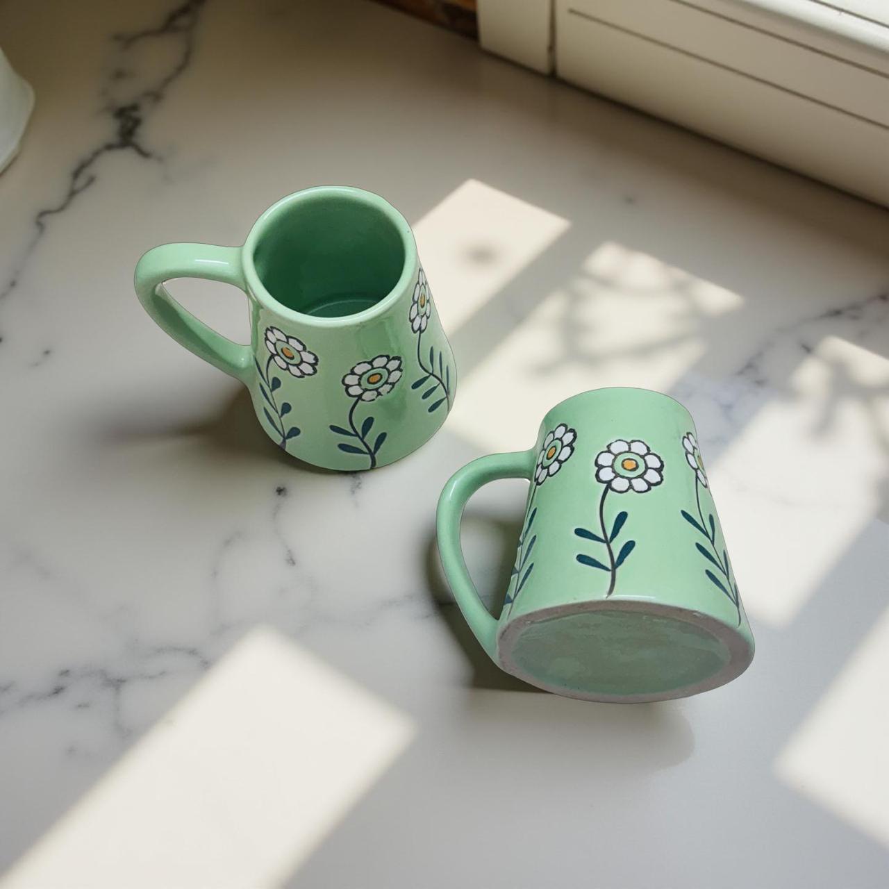 Two green mugs with floral designs on a marble surface.