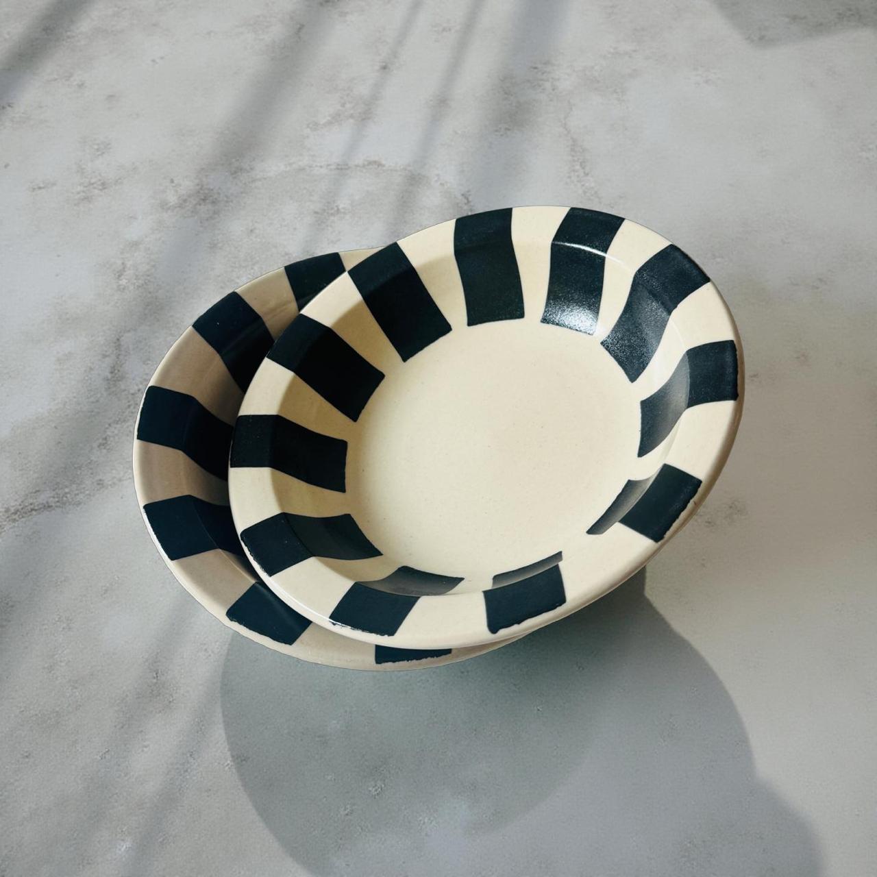 Ceramic bowl with black and white striped pattern on a concrete surface