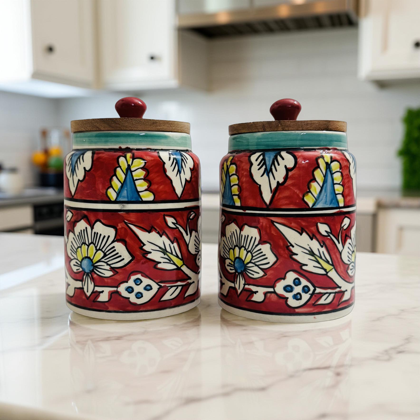 Set of two red floral handpainted ceramic jars with wooden lids on a kitchen counter