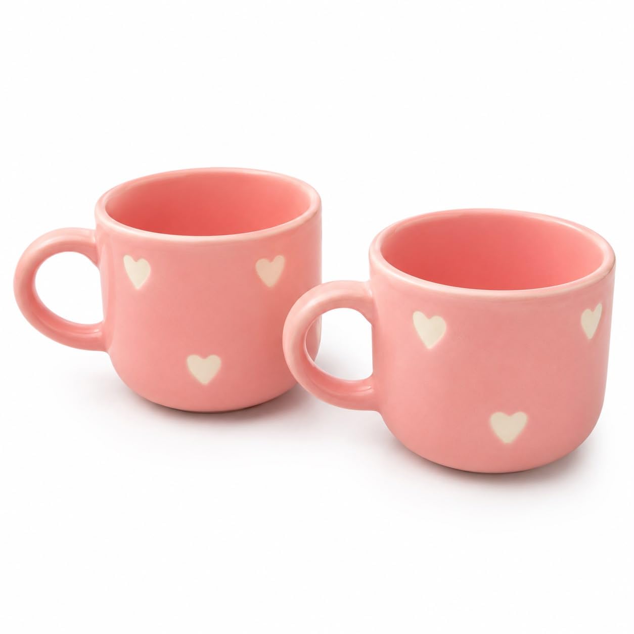 Two pink ceramic cups with small white heart patterns, shown on a clean white background.