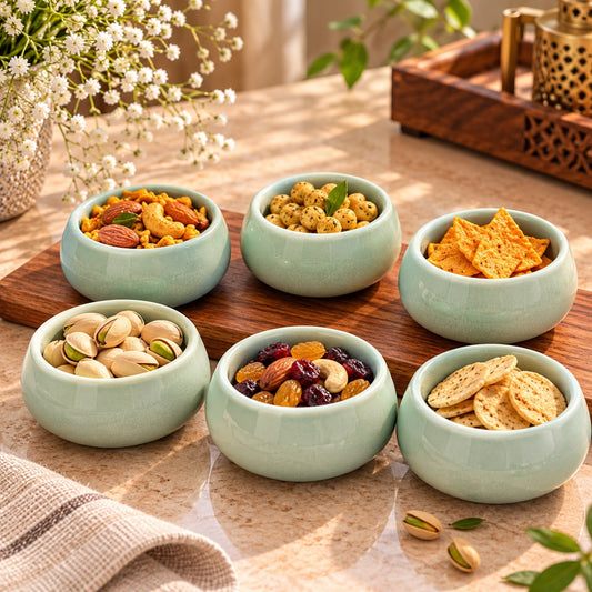 Set of six sage green ceramic bowls with a glossy finish, arranged on a wooden board and beige countertop for a warm kitchen display.