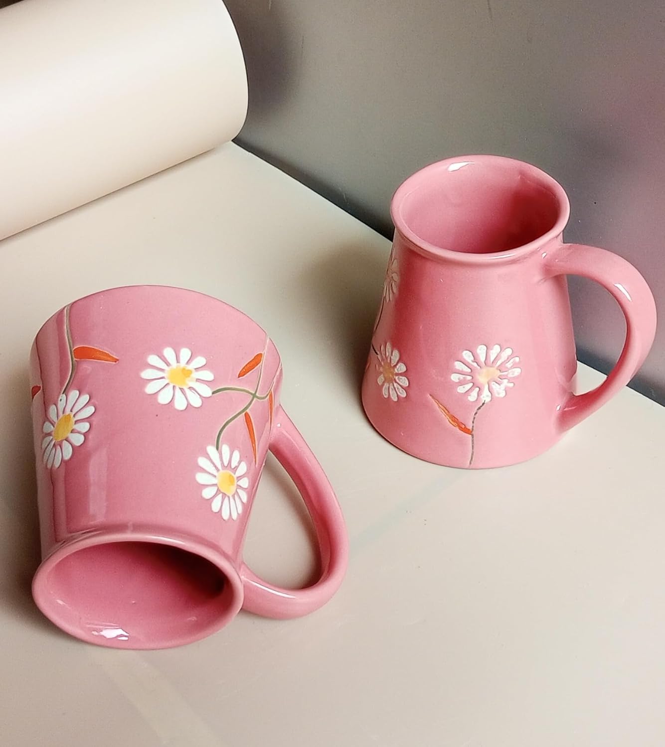 Two pink mugs with floral designs on a light surface.